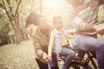 African American Father driving daughter on bike.