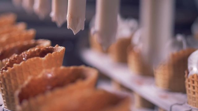 Close up of wafer cones getting filled with white substance for ice-cream