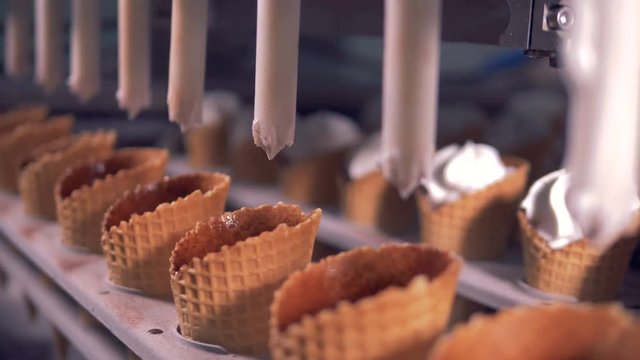 Ice-cream is being poured into waffle cones by automated tubes