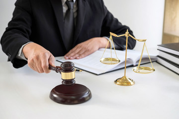Close up of Male lawyer or judge hand's striking the gavel on sounding block, working with Law books, report the case on table in modern office, Law and justice concept