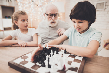 Grandfather, grandson and granddaughter at home. Grandpa teaches children how to play chess.