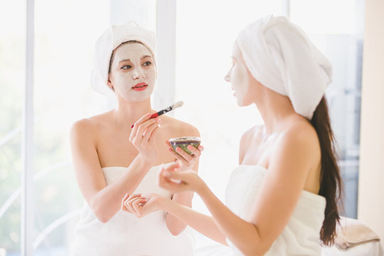Beautiful young woman and friend spa applying cosmetic mask cream on face relaxing receiving massage,Spa face concept
