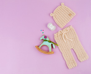 Hat and pants for newborn baby, dummy and toy horse gingerbread on violet background