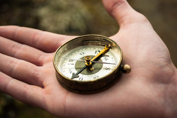Closeup of hand holding old,magnetic golden compass and showing directions in the woods