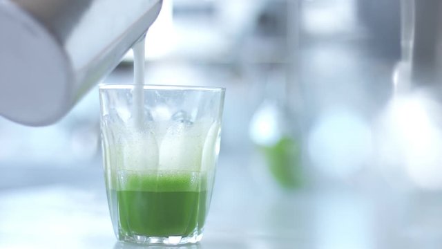 transparent glass with prepared matcha and milk pouring in it