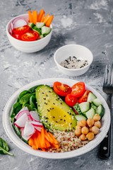 Green vegetarian buddha bowl salad with vegetables and quinoa, spinach, avocado, cucumbers, tomatoes, carrots, radishes, chickpeas with sesame seeds