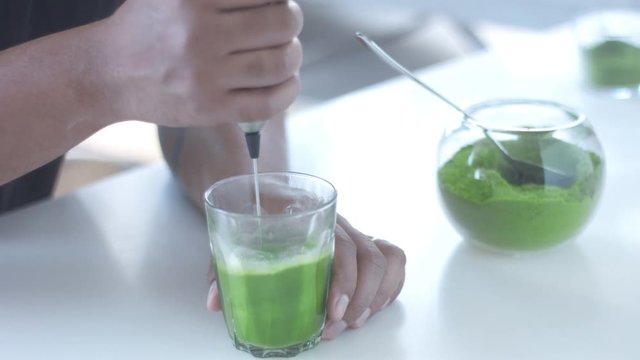matcha tee closeup mixing in transparent glass with electric mixer