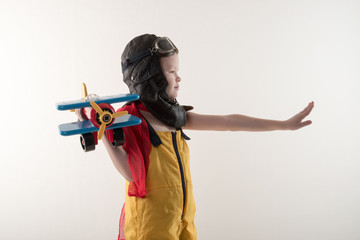 Funny boy in yellow overalls and  hat, in a red scarf and pilot's goggles, sits on vintage suitcase with an airplane model and dreams of adventures. The concept of travel romance and discovery