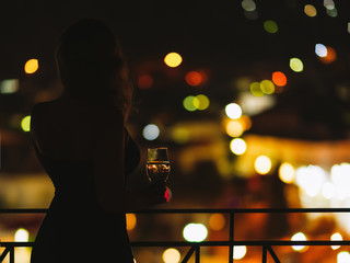Silhouette of  woman on the balcony with a glass of wine on the background of a night city