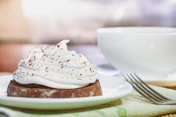 A chocolate cake with egg white cream, a cup of hot tea and a fork on a wooden table