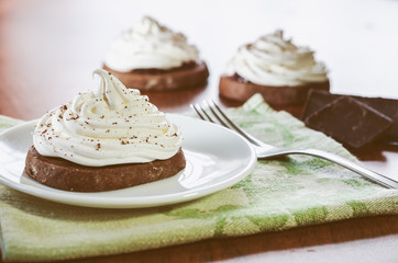 Chocolate cakes with egg white cream, pieces of chocolate and a fork on a wooden table