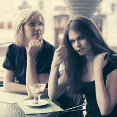 Two young women eating an ice cream at sidewalk cafe