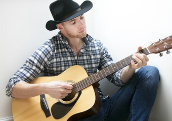 Handsome Country & Western cowboy playing guitar in hotel room 