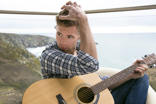 Handsome man, musician playing guitar on hotel balcony