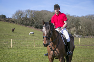Rider on Horseback in field, wearing red polo shirt, white trousers,  black boots with horses in the background