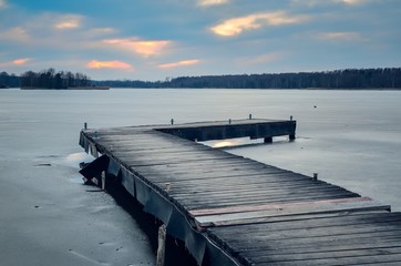 Evening winter landscape. Wooden pier over a beautiful frozen lake.