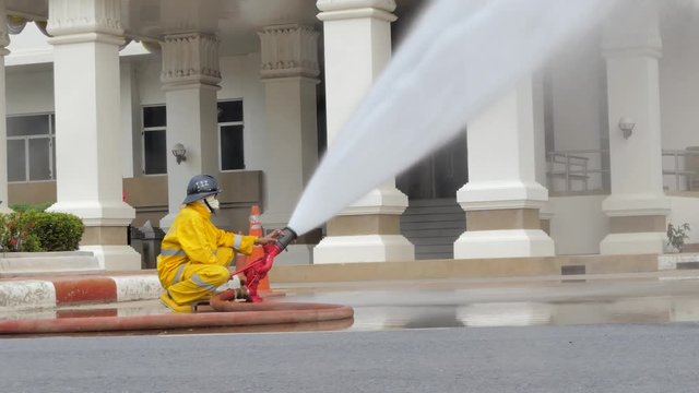 Firefighter water spray by high pressure fire hose into areas affected by fire