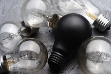 Fototapeta premium Burned light bulbs and one black light bulb on a gray concrete background.