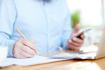 Male holding pencil over document while making notes and browsing in the net