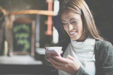 Smiling  young girl sitting in cafe and using smart phone.