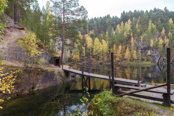 Lake with a shore covered with autumn forest, bridge over the river. quarry talc stone