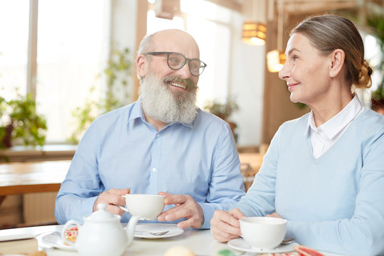 Happy senior man and woman enjoying time and talk in cafe by cup of tea or coffee
