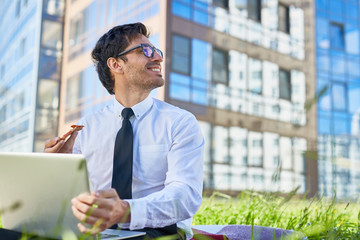 Fototapeta premium Young businessman looking at sky on summer day while networking and having pizza in urban environment