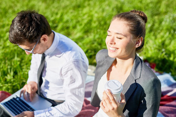 Young businesswoman with drink enjoying sunshine while her colleague networking near by