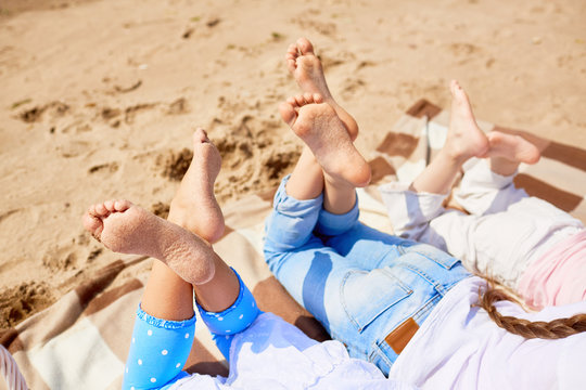 Soles Of Bare Feet Of Girls Lying On Sandy Beach On Hot Summer Day And Enjoying Rest