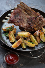 Close-up of roasted lamb meat on bone served with potato wedges and sauce, vertical shot, selective focus