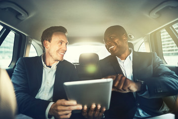 Smiling colleagues working online together in a car backseat