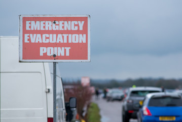 emergency evacuation point sign with cars leaving in background during coronavirus outbreak