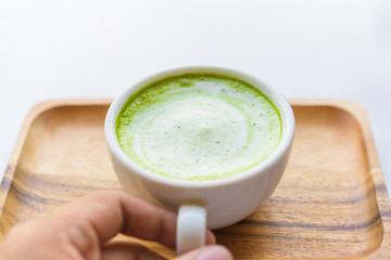 Matcha green tea latte beverage in glass on wooden table.