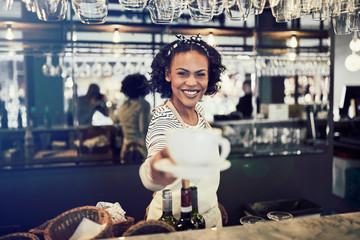 Young barista smiling and offering up a cup of coffee