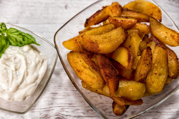 Roasted potatoes with herb sauce in glass dish placed on wooden table traditional European food