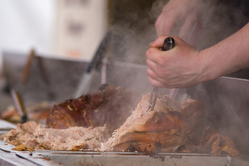 man carving pork joint with fork and knife at hog roast