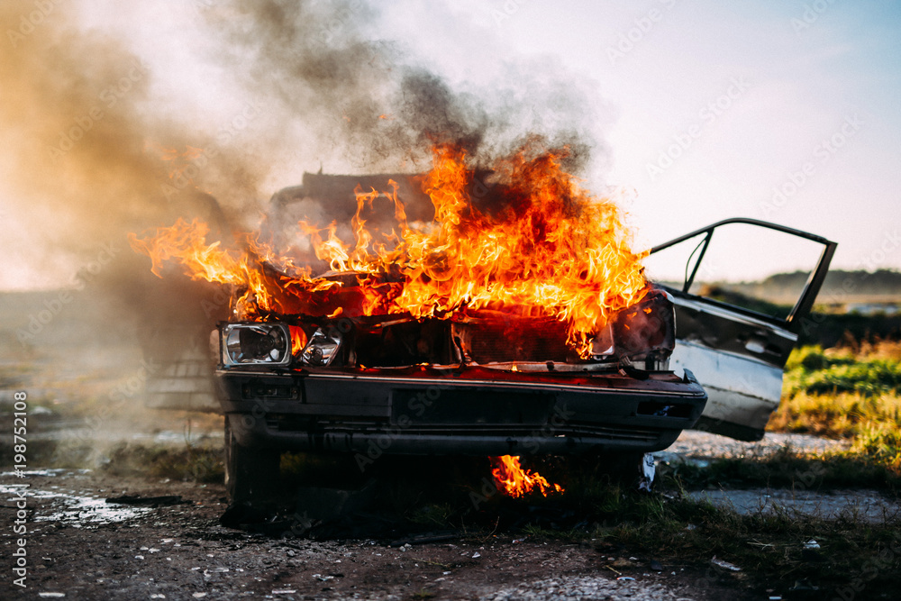 Wall mural front of a car burning with a open flames and dark smoke