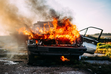Front of a car burning with a open flames  and dark smoke