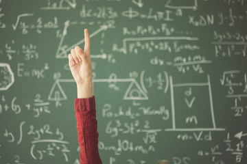 Student raised up hand pointing finger in front of green chalk board