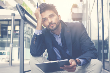 Fototapeta premium Serious businessman sitting on city street and holding document.