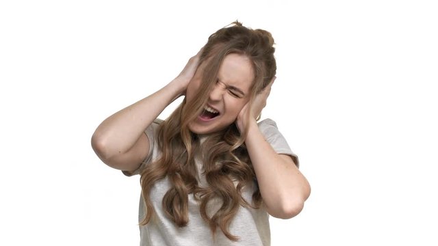 Portrait of long-haired woman 20s covering ears while screaming due to annoying noise or scary situation, isolated over white background closeup. Concept of emotions