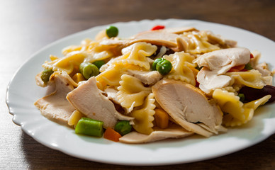 farfalle pasta salad with chicken breast fillet and vegetables in plate on wooden background