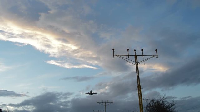 Airplane flying above a lamp posts a cloudy day at sunset