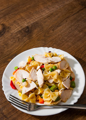 farfalle pasta salad with chicken breast fillet and vegetables in plate on wooden background