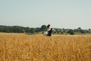Wedding couple is spinning in the summer wheat field. Bride in white puffy dress hold groom's hands...