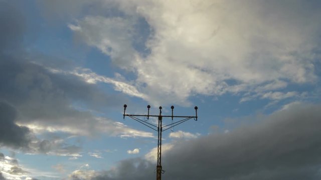 Airplane passing above a airport lamp posts a cloudy day at dusk