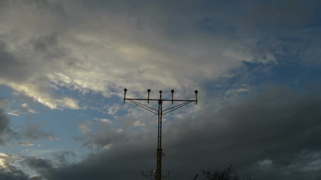 Airplane passing and arriving to airport above a lamp posts a cloudy day at sunset