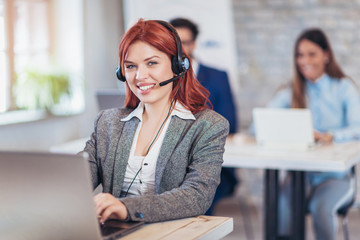 Portrait of happy smiling female customer support phone operator at workplace.