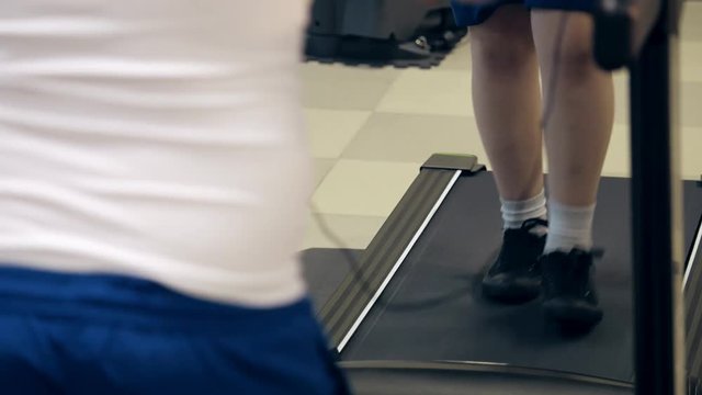 legs of fat boy in sneakers walking on treadmill during cardio workout in gym indoors
