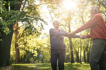 Smiling senior couple in forest holding hands and rotate in circle.